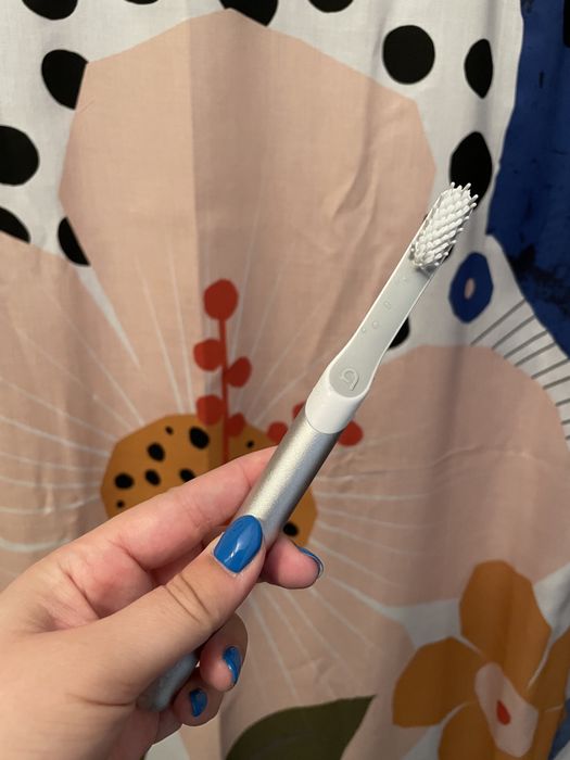A Mytourer is holding a silver Quip toothbrush in their hand.