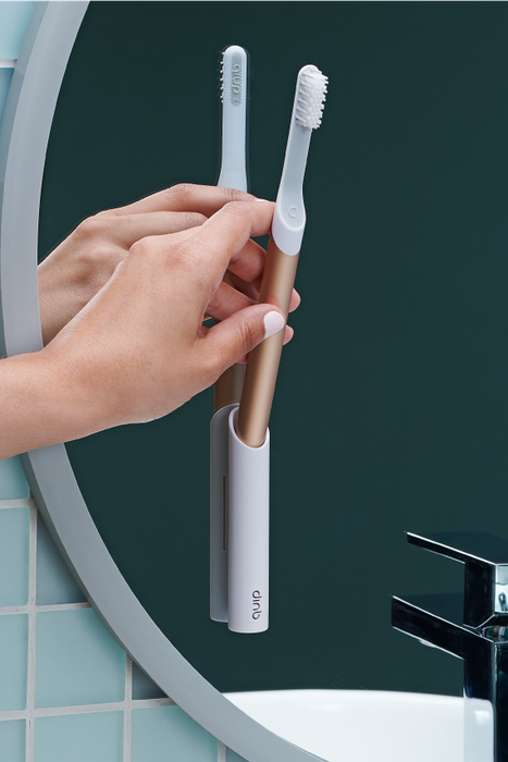 A model is positioning a rose gold toothbrush into a stick-on caddy.