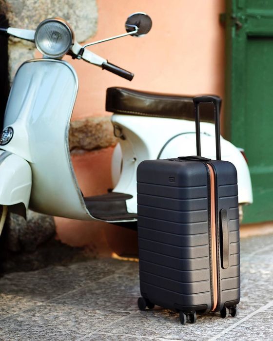 A navy blue Away suitcase placed next to a Vespa.