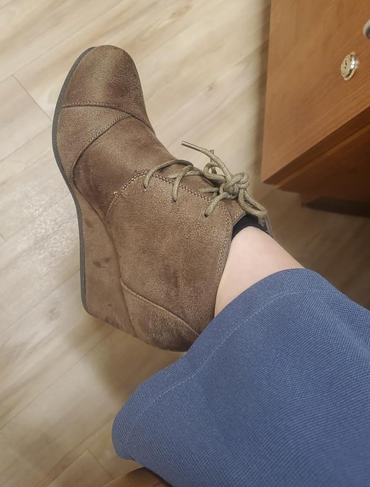A pair of brown suede wedge ankle boots featuring lace-up detailing, paired with stylish blue trousers.