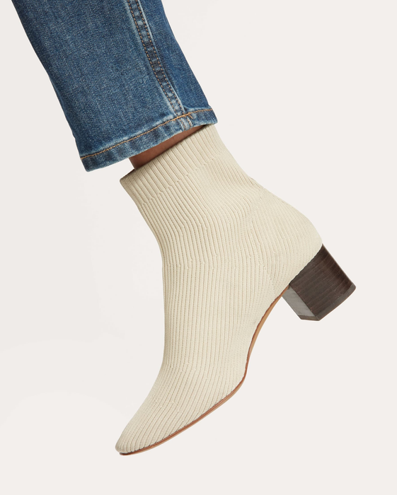 Close-up of a foot dressed in a cream-colored ribbed sock boot featuring a block heel, paired with denim jeans.