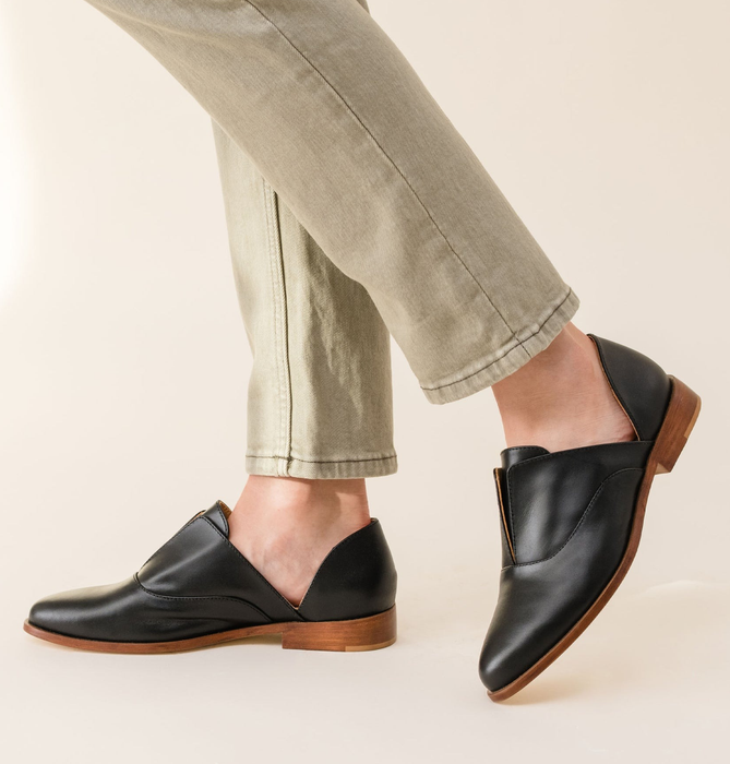 A person sports stylish loafers with a polished look and wooden soles, paired effortlessly with casual trousers.