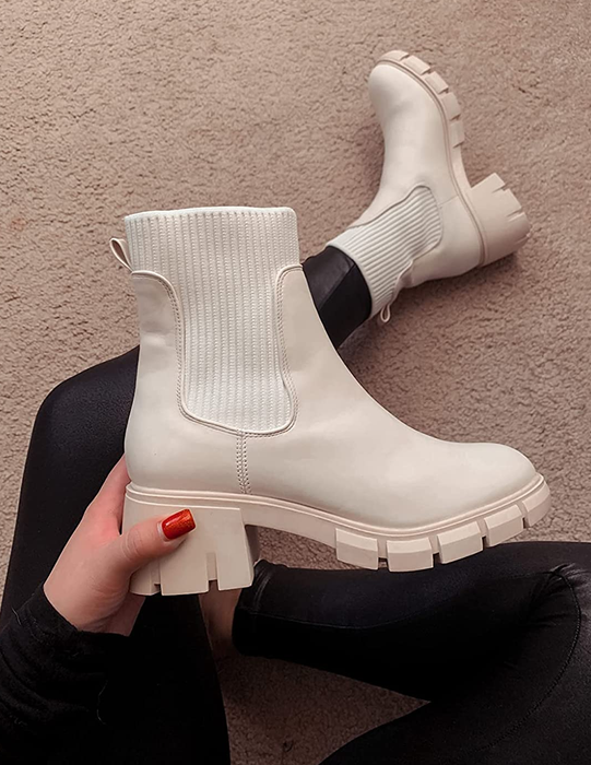 A reviewer sporting one of the platform Chelsea boots and holding the matching white counterpart.