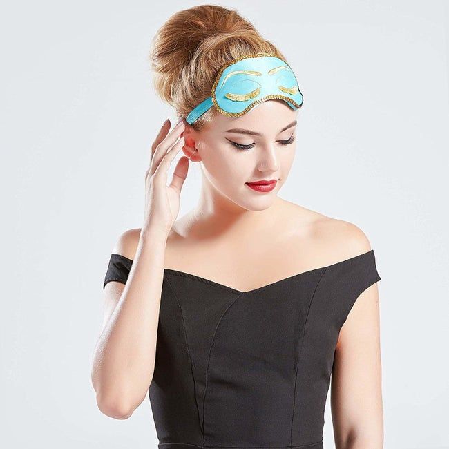 A model wearing the blue eye mask with gold trim, embroidered closed eyes, and fringed lashes