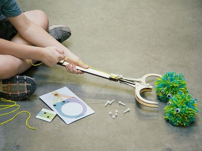 A model reaching for a pair of fluffy balls using a claw hook