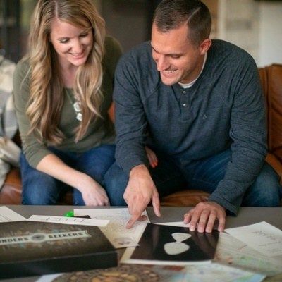 Two people smiling over a coffee table, surrounded by papers and a Finders Seekers box.