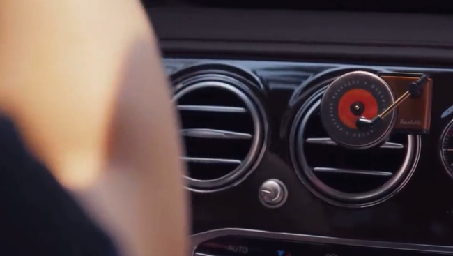 A car dashboard featuring a circular air freshener attached to a vent, with a person sitting inside the vehicle