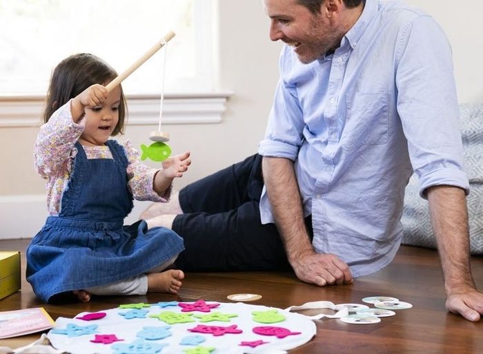 An adult model smiling as a child model plays with an interactive indoor fishing set