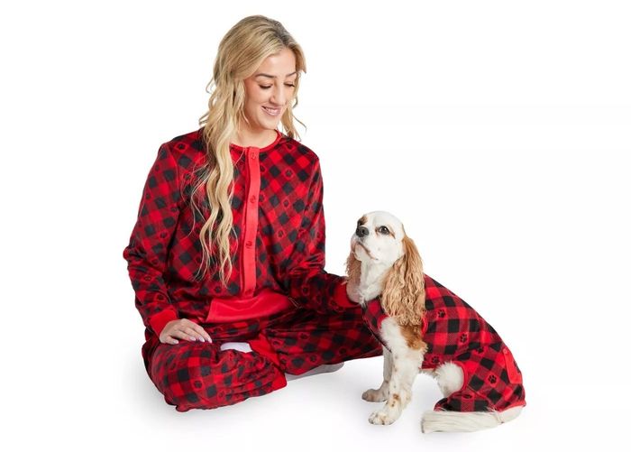 A person and their dog, both sporting matching plaid pajamas. The person is seated, smiling at the dog, in a shopping article.