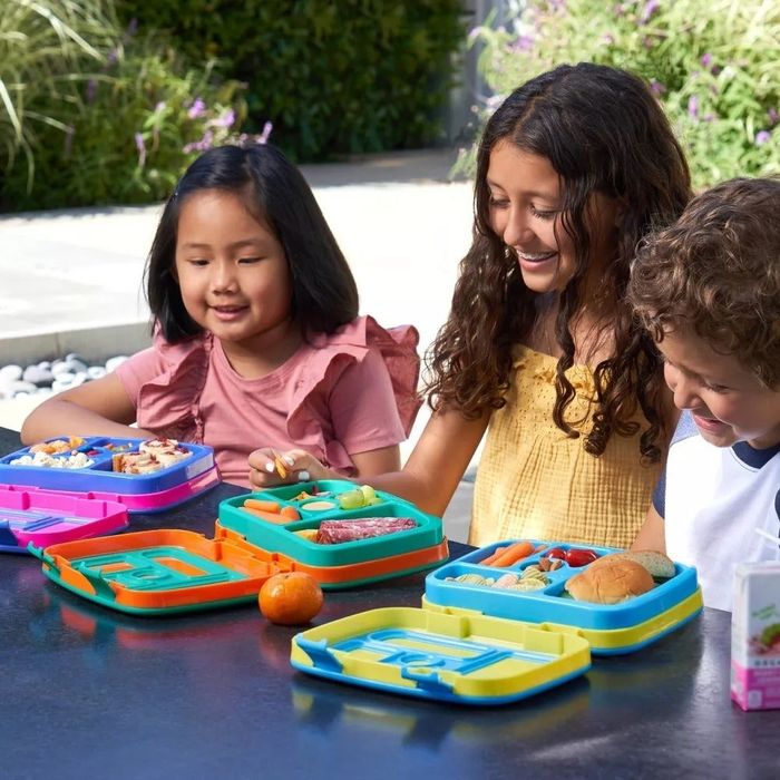 Three children joyfully eating from Bentgo lunchboxes outdoors.