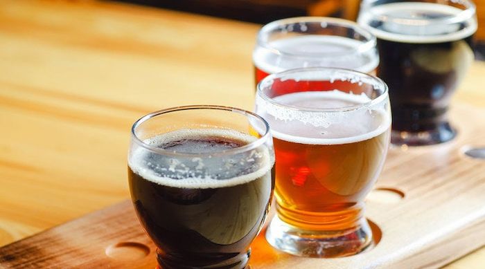 A flight of various craft beers served in small glasses on a wooden table in a pub.