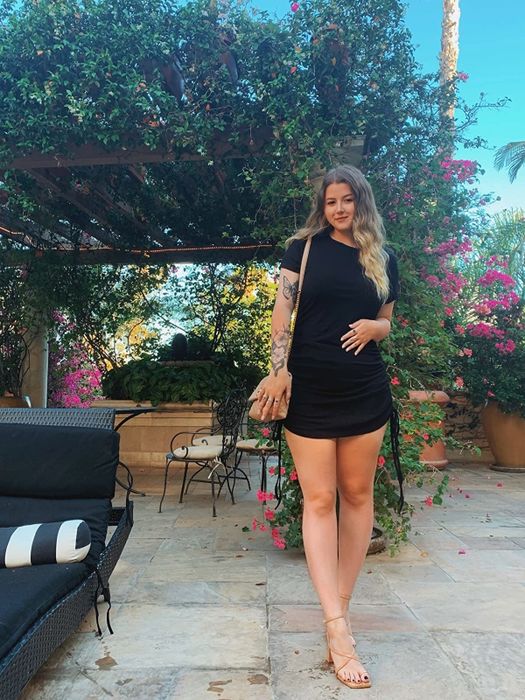 A reviewer is wearing a sleek black short-sleeve bodycon dress.