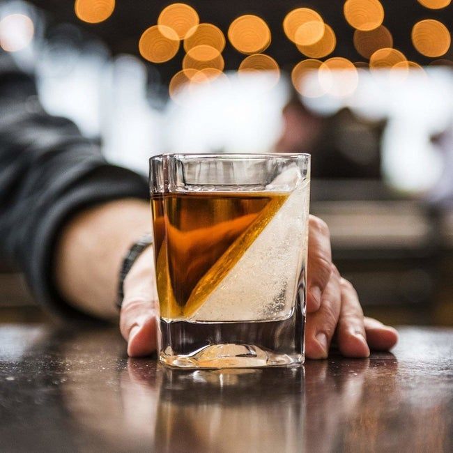 A rocks glass filled with a wedge of ice and a splash of brown liquor