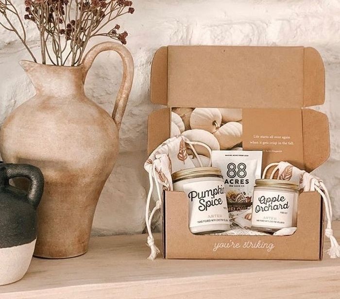 Two candles nestled in an open cardboard box beside a vase.
