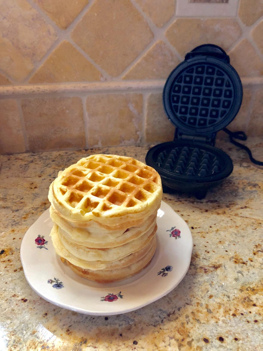 A reviewer's waffle maker placed beside a stack of Eggo-sized waffles