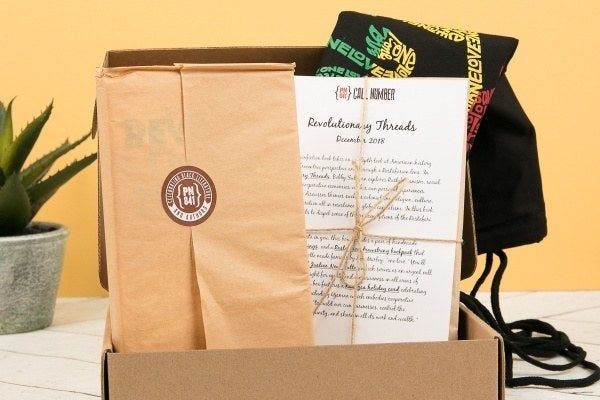 An open box containing a wrapped book, a tote bag, and a stack of documents.