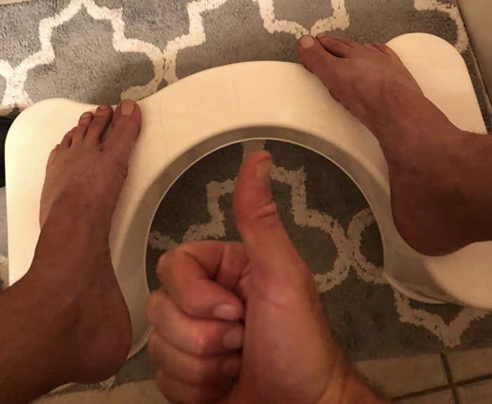 A customer review photo showing them giving a thumbs up while their feet rest on the Squatty Potty, placed beside their toilet