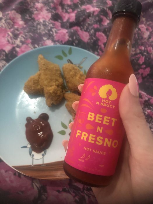 A bottle of hot sauce next to a serving of crispy chicken nuggets.