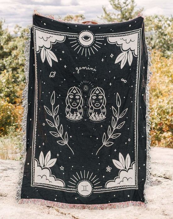 A sleek black throw blanket with fringe detailing along the edges, adorned with a celestial zodiac pattern for Gemini.