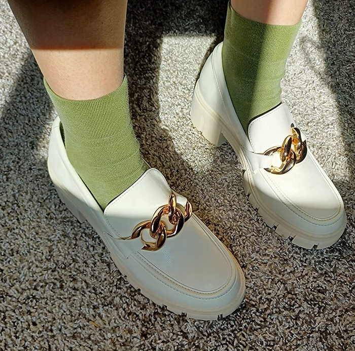 A reviewer showcases their white loafers paired with green socks, highlighting the footwear's distinct style.