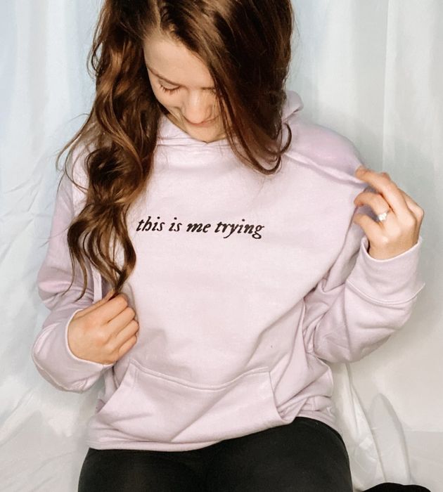A model wearing a light pink hoodie with the phrase 