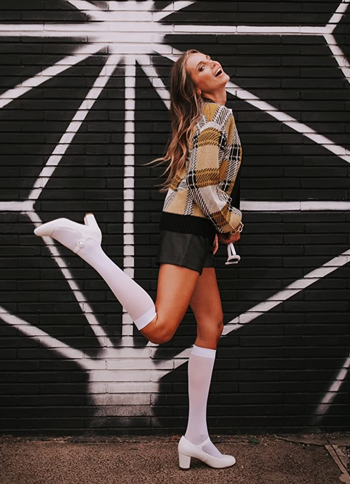 A reviewer models the white Mary Janes paired with knee socks.