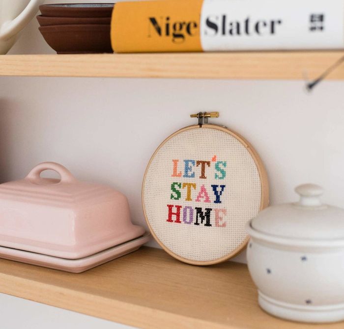 A colorful cross-stitch on a shelf that reads 