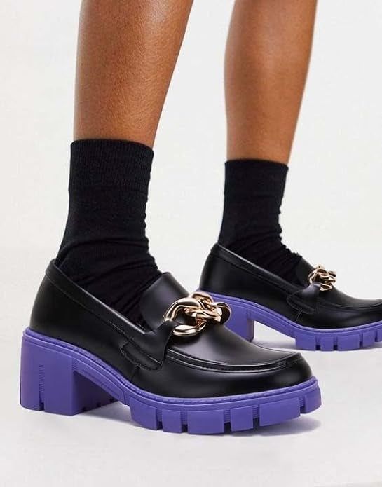 A person strikes a pose wearing chunky loafers with chain accents, standing confidently as a fashion-forward example for a shopping trends article.