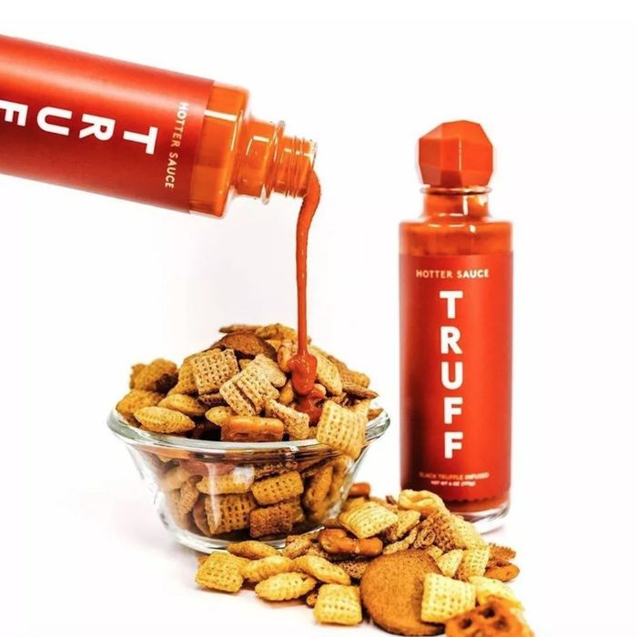 The truff hot sauce being poured onto a bowl of Chex Mix.