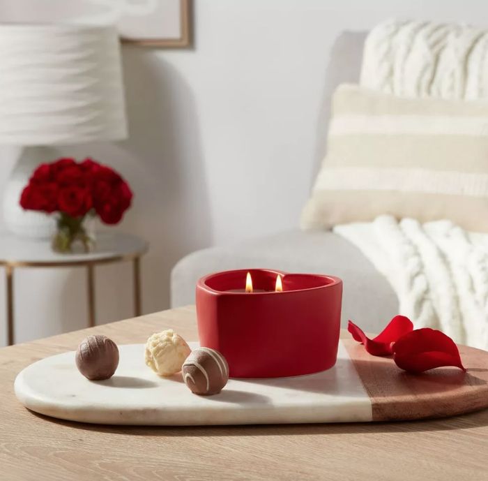 the red ceramic heart-shaped candle glowing on a table beside chocolate treats