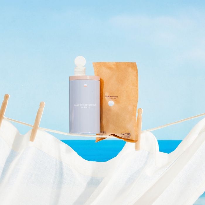 The tin containing laundry tablets is placed alongside a bag of laundry tabs on a drying line.