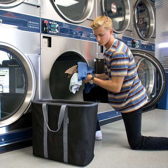 A person is taking items out of the laundry tote to load into a washing machine at the laundromat.