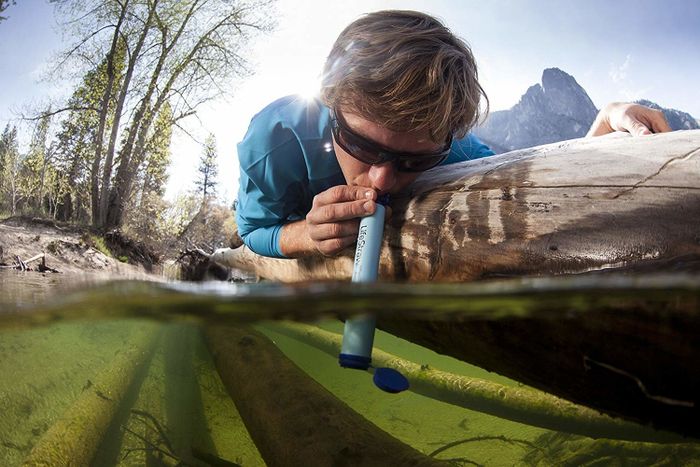 A person drinking from a seemingly dirty stream using a Lifestraw.