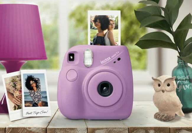 A purple Instax Mini 7+ camera printing a photo of two friends