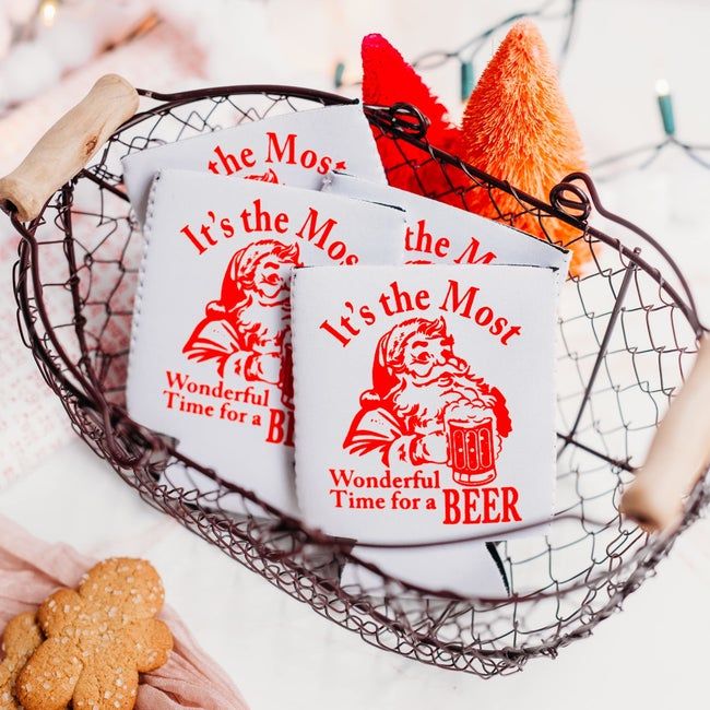 A basket filled with white coozies featuring Santa, with the phrase 'It's the most wonderful time for a beer'