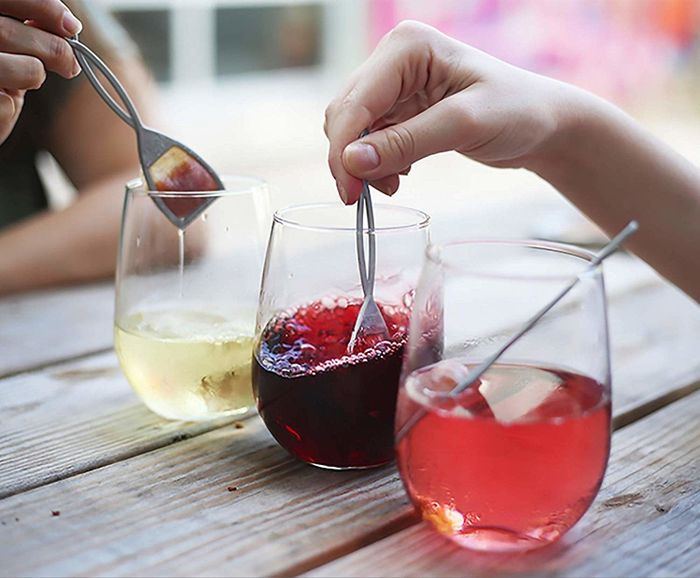 Hands dipping tea bag-like devices into wine.