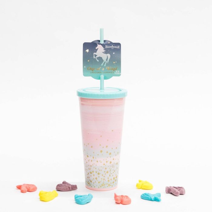 The tumbler features a soft pink hue with accents of light blue and white patches, complemented by gold glitter specks. It also comes with a light blue lid and straw.