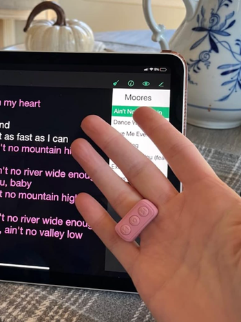 A hand holding a pink controller in front of a tablet displaying song lyrics.