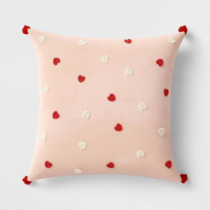 This square blush pillow features small red pom-poms at each corner and is adorned with delicate red and white beaded hearts.