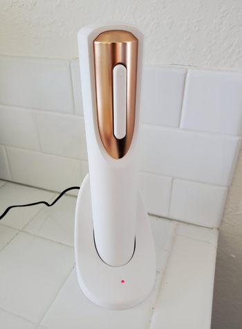 A cordless automatic wine opener placed on a white countertop, with a charging base beside it.
