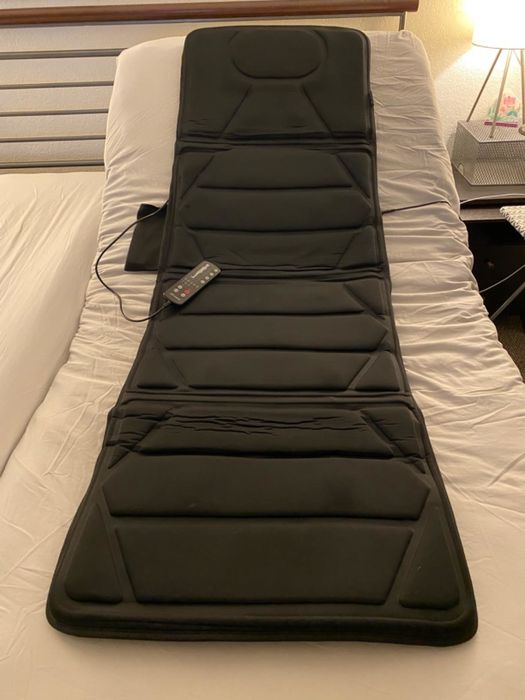 A massage mat with a remote control placed on a bed, designed to offer relaxation and comfort for the user.