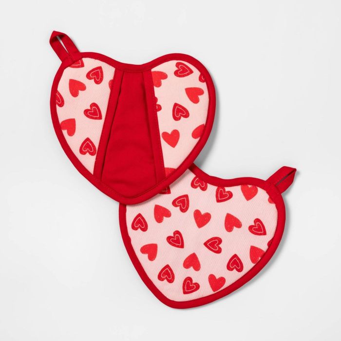 These heart-shaped pot holders feature a red fabric on one side, complete with a shallow hand pocket, and pink fabric on the other side adorned with red heart prints.