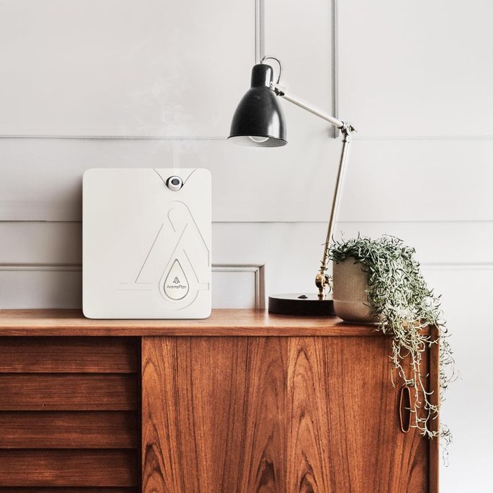 A sleek, modern air purifier resting on a wooden sideboard next to a potted plant and beneath an adjustable lamp.