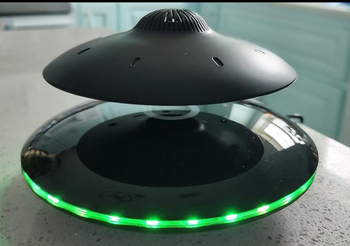 A levitating speaker illuminated with green LED lights.