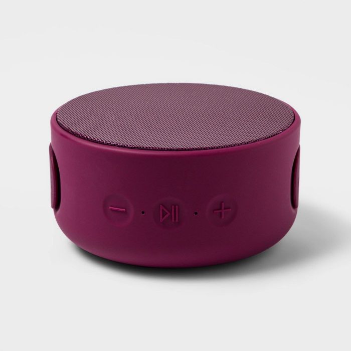 The speaker, compact and round, in a vibrant raspberry color.