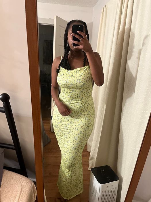 A reviewer showing off the same backless maxi dress in a green color with a blue floral print.