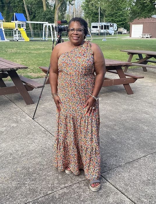 A reviewer wearing a vibrant floral-print one-shoulder maxi dress