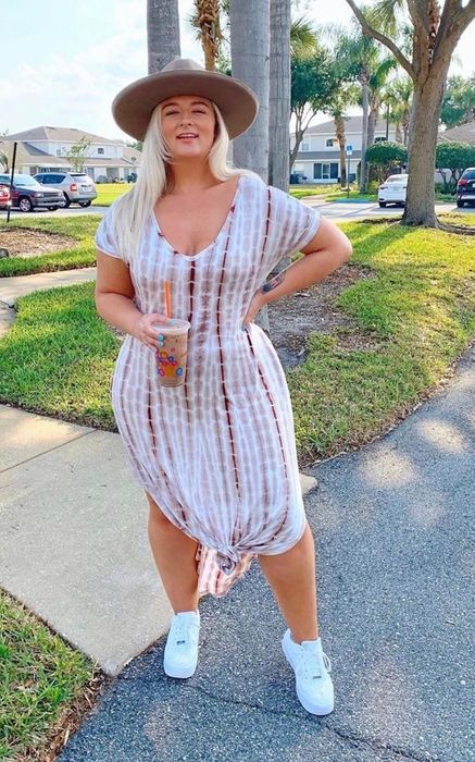 A reviewer wears the dress in a pink tie-dye pattern, accessorized with sneakers and a hat.