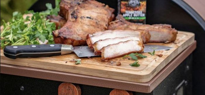 The bamboo cutting board features a large knife, some meat, and greens placed on top of it.