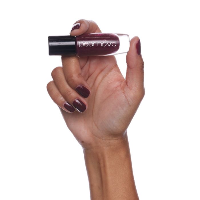 A model holding up a maroon bottle of Pear Nova nail polish, showcasing its rich color and elegant finish.